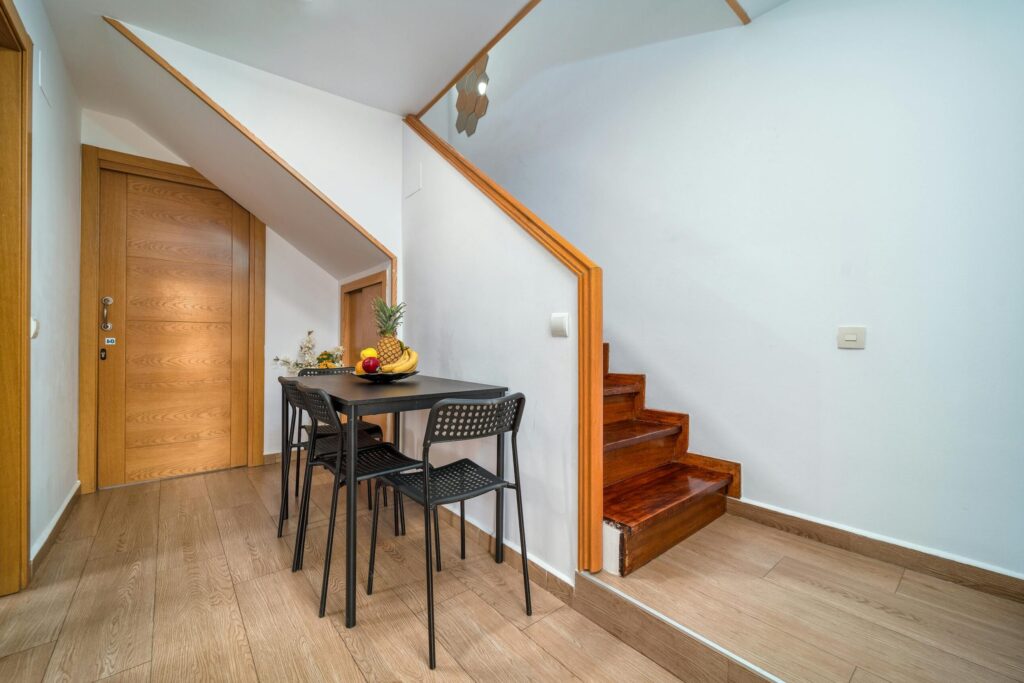 Clean and minimalist interior with wooden accents, featuring a small dining area under the stairs.